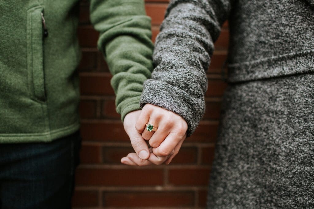 Brown Goldsmiths Olympia Ring in yellow gold with a green Tourmaline on a hand - Couple holding hands Brown Goldsmiths Olympia Ring in yellow gold with a green Tourmaline on a hand - Couple holding hands